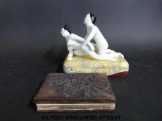 A ceramic erotic model of a couple on a yellow cushion (length 18cm) together with a wooden-bound