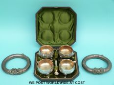 Two white metal slave bangles and a cased set of four silver plated salts