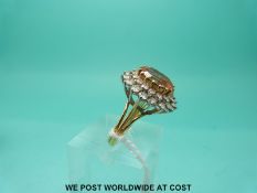 A yellow metal ring set with an oval cut golden topaz surrounded by two rows of diamonds (size O)