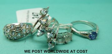 Four silver rings including one set with three square cubic zirconia, one set with blue topaz,