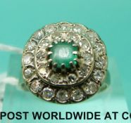 A white metal ring marked 18k set with an emerald surrounded by two rows of diamonds (size M)