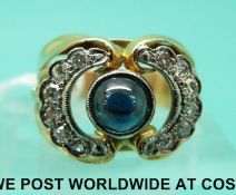 A yellow metal ring set with a sapphire cabochon and two half circles of diamonds,