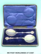 A pair of cased hallmarked silver Arts and Crafts serving spoons with decorative finials,
