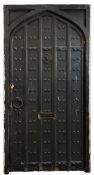 A Gothic pointed arch and black painted and iron studded panelled door:, in a softwood frame,