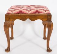 A walnut stool of George I design:, with an upholstered needlework slip in seat and shaped apron,