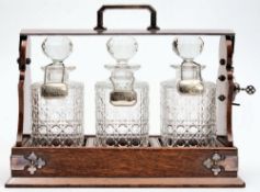 An oak and electro-plate mounted tantalus: containing three clear cut glass decanters and stoppers