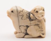 A Japanese carved and stained ivory netsuke: of two playing dogs,