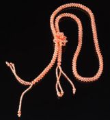 A pink coral bead rope necklace: with stylised floral cluster and two tassels.