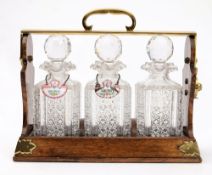 A Betjemanns Patent oak and brass mounted tantalus: containing three cut glass decanters and