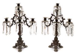 A pair of Continental iron and glass lustre twin branch candelabra: the foliate nozzles of