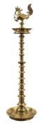An Indian Deccan brass oil lamp: with cockerel finial and reservoir below,