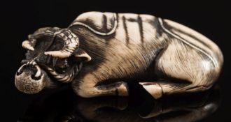 A 20th century Japanese carved ivory and stained netsuke of a reclining oxen: with a rope tied to