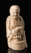 A Japanese carved ivory figure of an actor: modelled as a male kneeling figure holding a Noh mask,