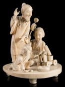 A Japanese carved ivory okimono of a mask maker and family: with wife and child kneeling on the