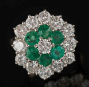 An emerald and diamond mounted circular cluster ring: with a central brilliant-cut diamond