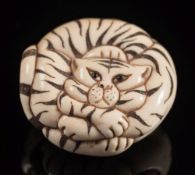 A Japanese carved ivory netsuke of a tiger: curled up, with inset eyes, having stained stripes,