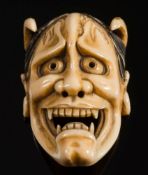 A Japanese carved ivory okimono of a Hannya Noh mask: with pierced eyes and nose, protruding horns,