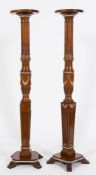 A pair of carved satinwood and decorated torchere stands:, with circular moulded tops on reeded,