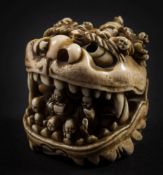 A Japanese ivory okimono in the form of a mythical beast's head: with a host of small figures on