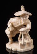 A Japanese carved ivory okimono: of a peasant wearing a straw hat, holding a basket and a spade,