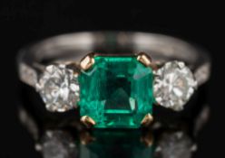 An emerald and diamond three-stone ring: with central square 'emerald-cut' emerald approximately