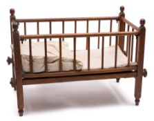 An Edwardian doll's crib: with turned spindle drop sides, raised on four peg feet, 61cm. long.