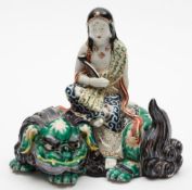An Arita porcelain figure group: modelled as Manjusri seated wearing lose robes and holding a ryui