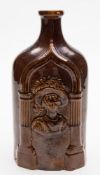 A mid 19th century brown glazed pottery gin flask: modelled on either side with head and shoulder