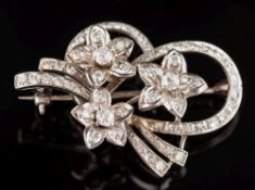 A diamond mounted floral spray brooch: with three flower heads and ribbon scroll pave-set with old