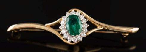 An emerald and diamond mounted bar brooch: the central oval emerald 10mm long x 8mm wide,