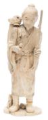 A Japanese carved ivory sectional okimono of a peasant: standing with a staff in one hand and