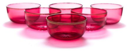 A set of six cranberry glass finger bowls: of circular form with star cut bases and gilt rims,