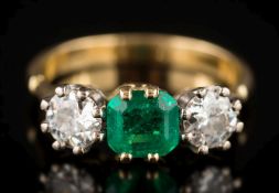 A yellow gold, emerald and diamond three-stone ring: the central emerald-cut emerald 6.2mm long x 5.