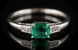 An emerald and diamond three-stone ring: the rectangular emerald approximately 0.