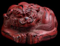 A Japanese red lacquer netsuke and a carved horn netsuke: the first in the form of a sleeping tiger,