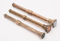 Three late 19th/early 20th century yellow metal propelling pencils:, with engraved hexagonal shaft,