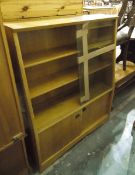 Modern glazed bookcase with three shelves enclosed by sliding doors and cupboard under