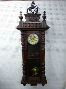 A WALNUT CASED VIENNA STYLE WALL CLOCK, the pendulum driven movement set behind an enamel dial