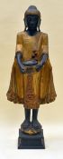A FLOOR STANDING PAINTED WOODEN BUDDHIST FIGURE holding a vessel before him and stood upon a