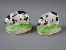A PAIR OF RECUMBENT STAFFORDSHIRE POTTERY RABBITS on oval grassy bases, 19th Century, 8 cms long