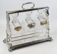 A GOOD QUALITY THREE BOTTLE EPNS TANTALUS raised on bun feet and decorated with vines to the body,