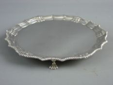 A SILVER CARD TRAY ON THREE HOOF FEET, 19 cms diameter with rope and shell decorated border,