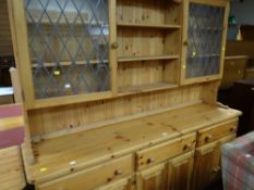 A modern pine dresser composed of three drawers and cupboards to the base and having a semi-glazed