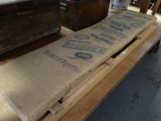 A long narrow folding wooden garden bench with sacking covered cushion