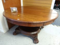 An antique circular two sectioned mahogany dining table with central support and lion claw feet