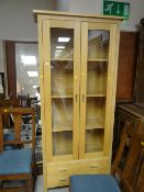 A modern light oak two-door display cabinet with a two-drawer base