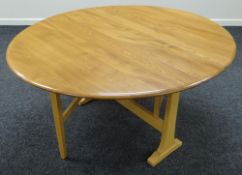 An Ercol drop leaf oval dining table in blonde, 120cms diam