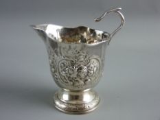 A CIRCULAR BASED SILVER CREAM JUG with raised fruit and floral decoration, crest to the front and