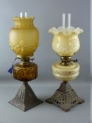 TWO VICTORIAN OIL LAMPS, both on iron bases, one with amber glass reservoir and similar coloured