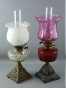 TWO VICTORIAN OIL LAMPS with iron bases, one with cranberry glass reservoir, the other clear